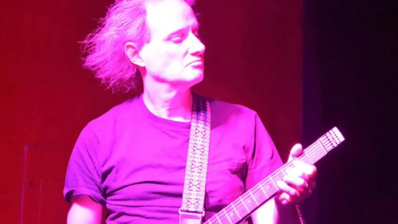 Dark red and fushia stylized image of man playing guitar