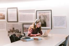 Student wearing white headphones studying at computer in lobby