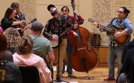 Students with folk-style string instruments playing for a seated audience.