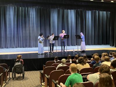 Flute quartet performing on stage to audience of students