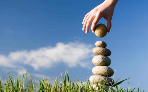 A hand stacking round rocks on grass