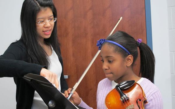 Student teaching giving violin lesson to young child