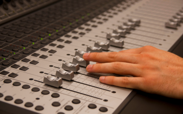 Person's hand adjusting faders on mixing console