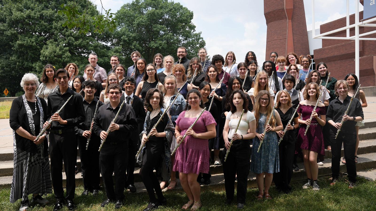 Students in recital attire posing with flutes outdoors