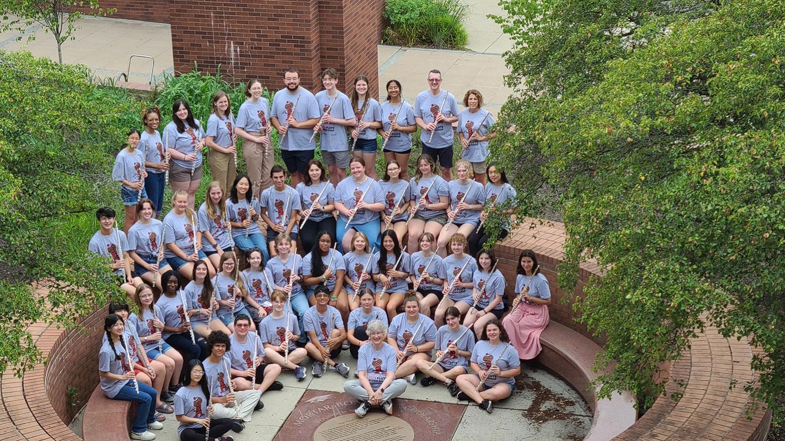 50 students in gray Flute Workshop t-shirts posing with their flutes outdoors