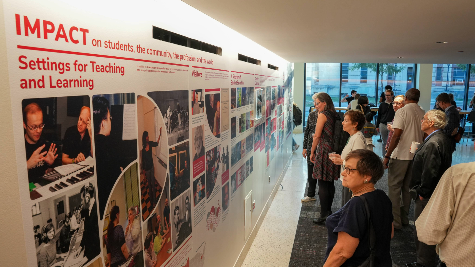 Crowd of people viewing wall with photo mural depicting 100 years of the School of Music
