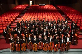 Orchestra posed with instruments in red seats of Weigel Auditorium