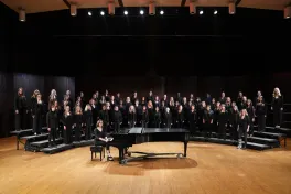 Women's Glee Club posed on risers on stage with grand piano in front